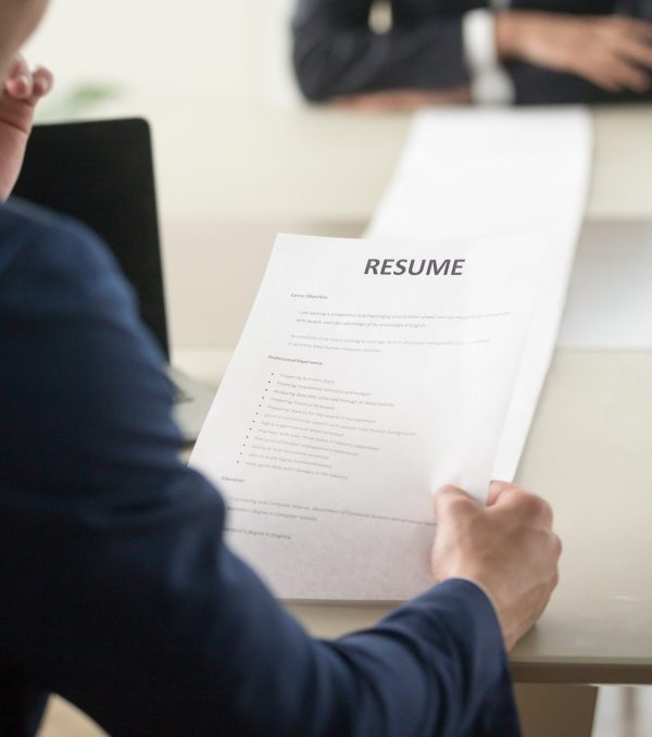 Back view of employer reading resume focus on document, job applicant waiting for hiring decision at desk on background. Hiring manager studying long list of candidates achievements and experiences