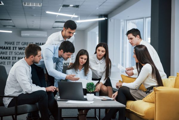 Guy shows document to a girl. Group of young freelancers in the office have conversation and working Guy shows document to a girl. Group of young freelancers in the office have conversation and working.
