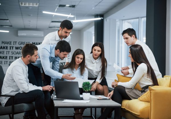 Guy shows document to a girl. Group of young freelancers in the office have conversation and working.