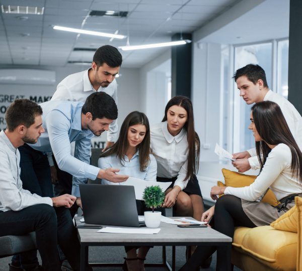 Guy shows document to a girl. Group of young freelancers in the office have conversation and working.