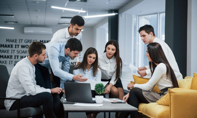 Guy shows document to a girl. Group of young freelancers in the office have conversation and working.